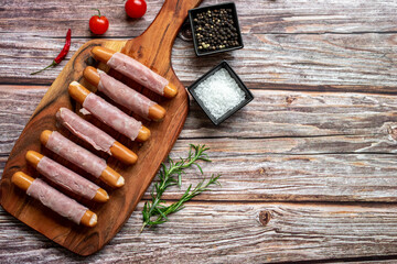 raw sausages wrapped in bacon on a wooden background with copy space for your text