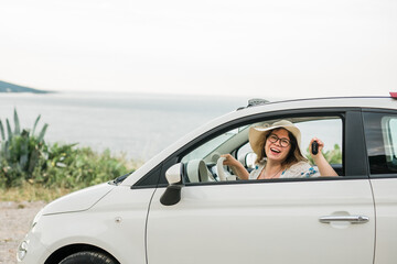 Car driver woman smiling showing new car keys and car copy space. Female driving rented cabrio on summer vacation