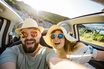 Romantic couple making selfie on smartphone camera in rental cabrio car on ocean or sea beach enjoying summer vacation together and taking picture on cellular resting near sea on weekends - obrazy, fototapety, plakaty