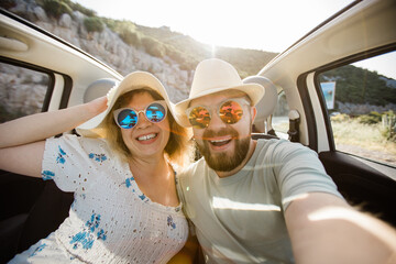 Romantic couple making selfie on smartphone camera in rental cabrio car on ocean or sea beach...