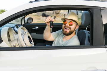 Car driver man smiling showing new car keys and car. Bearded guy driving rented cabrio on summer...