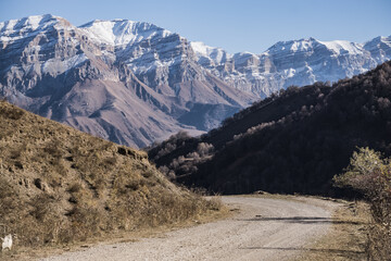 Road in the autumn mountains against the backdrop of a rocky ridge of mountain peaks with the first snow, sunny autumn day in the mountains landscape