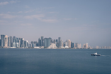 Naklejka premium doha skyline at day, skyscrapers standing tall and in line in the concrete jungle, and the small boat passing the gulf
