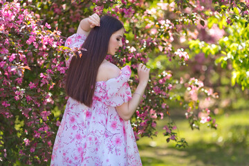 girl in a pink dress standing near pink blooming garden, rear view