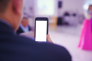 view from the back. a man shoots a video on a smartphone at a party.