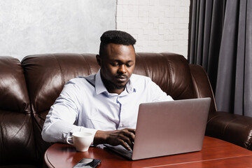 African american IT developer with laptop is programming code in office. African business man working on laptop and chatting with colleagues.