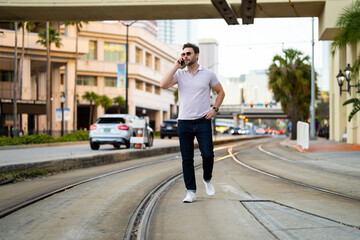 Young handsome man in classik polo t-shirt chatting on phone on the street. Handsome confident stylish hipster model talking on phone outside. Business phone conversation.