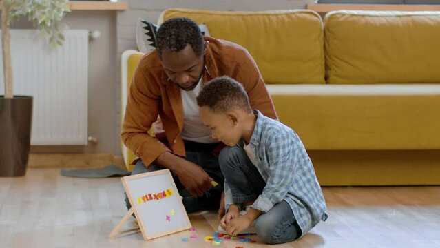 Early kids development. Caring black dad teaching his little son alphabet, cute boy putting magnetic letters on board