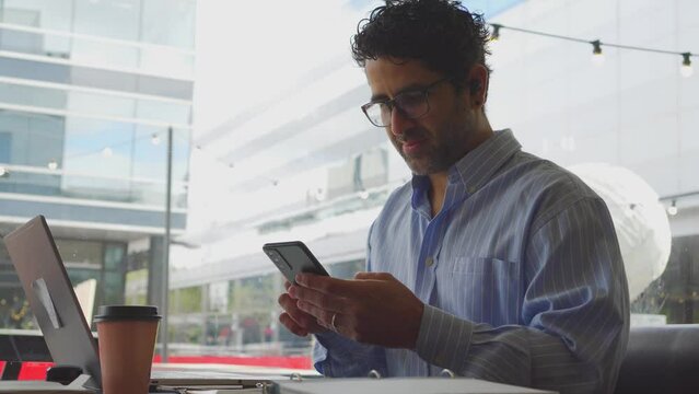 Middle-aged Latin man sending a text message on his cell phone while talking to a friend in a coffee shop. 4k video.