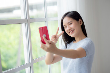 Happiness young asian woman video call with smartphone in the living room at home, female smiling and using social media online with smart phone at home, lifestyles and communication concept.