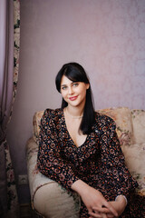 portrait of a beautiful young brunette woman in a dark dress in a home interior.