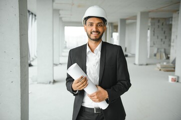 Indian construction site manager standing wearing helmet, thinking at construction site. Portrait of mixed race manual worker or architect.