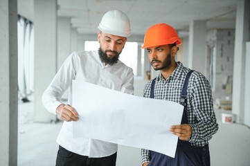 Multiracial male coworkers in hardhats discussing project on construction site