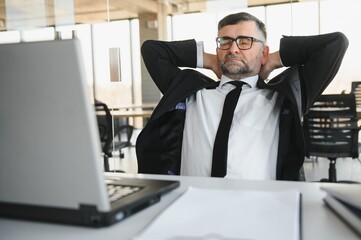 Tired stressed office worker sitting at desk and thinking, he is rubbing his eyes and feeling exhausted.