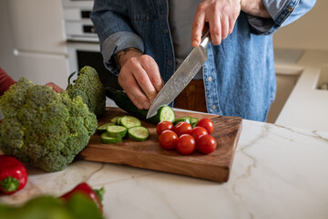 Close-up of a man cutting a cucumber, making a salad in his kitchen.