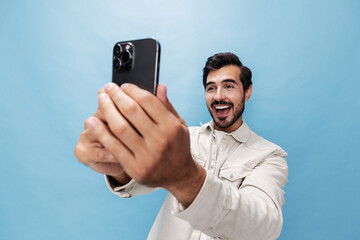Portrait of a stylish man brunette smile and open mouth looks at the phone blogger with a beard, on a blue background in a white T-shirt and jeans, copy space