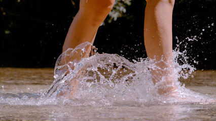 CLOSE UP: Barefoot woman splashing drops of water while crossing wild river