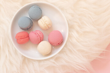 Clean pastel colored macaroon selection in top view. Luxury dessert selection on a white plate placed on a soft blanket.