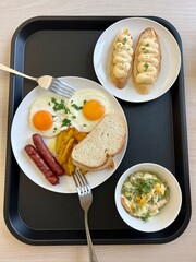 Delicious nutritious breakfast two sausages egg fried potatoes Bread salad with mayonnaise and two toast sandwiches with squirrel salad Stands on a tray in the dining room 2 forks all prepared for eat