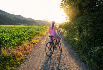 Woman on mountain bike on gravel road at sunset in summer