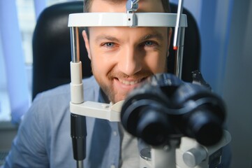 Handsome young man is checking the eye vision in modern ophthalmology clinic. Patient in...