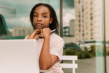 Serious calm face african american woman hipster sitting outside street cafe with laptop, working...