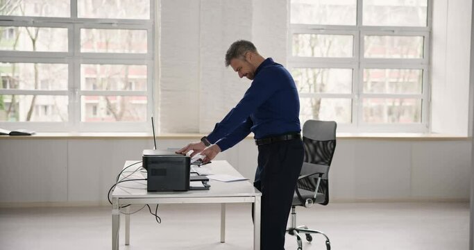 Irritated Businessman Looking At Paper Stuck In Printer