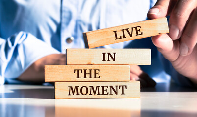 Close up on businessman holding a wooden block with "Live in the Moment" message