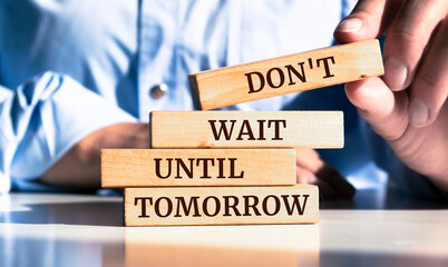 Close up on businessman holding a wooden block with "Don't Wait Until Tomorrow" message