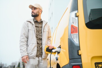 Casual man near electric car waiting for the finish of the battery charging process