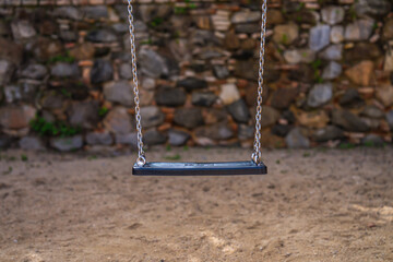 Lone black swing in a walled playground