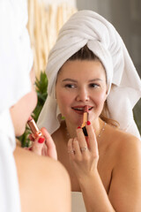 An attractive woman paints her lips with lipstick in front of the bathroom mirror. Make-up