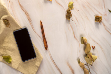 Still life with a smartphone on a cream-colored cloth, a pen, dry leaves on a marble surface