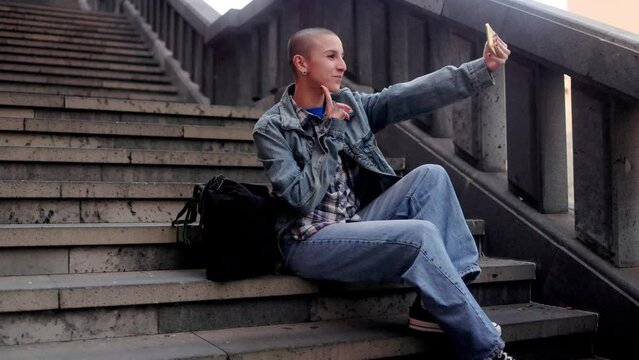 Bald young woman using mobile phone for streaming on social media outdoors in the city