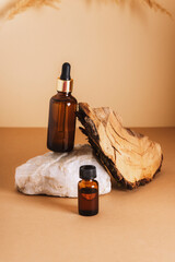 Brown cosmetic serum and essential oil bottles on a stone podium and wooden bark on neutral background. Natural skin care cosmetics concept. Closeup