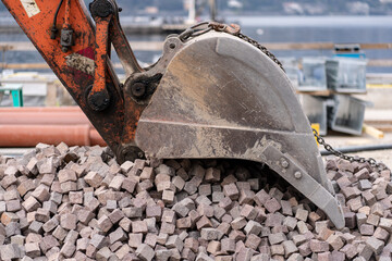 Excavator shovel placed on a pile of paving stones at a construction site at the port of Como.