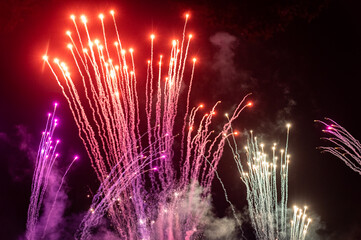 Pink, orange and white fireworks rockets in a dark sky with fiery tails. Smoke and fire with room...