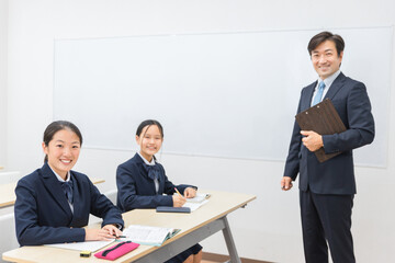 塾・学校の教室で先生に勉強を教わる小学生・中学生・高校生の子供（カメラ目線）
