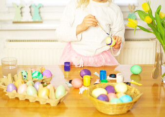 Fototapeta na wymiar A little girl painting eggs for Easter on the wooden table at home. Preparation for Easter.