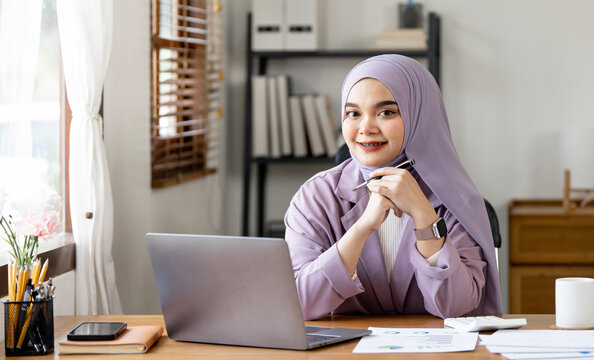 Portrait of Young Muslim Businesswoman Wearing Hijab Works on Laptop, Does Data Analysis, Looks at Camera and Smiles.