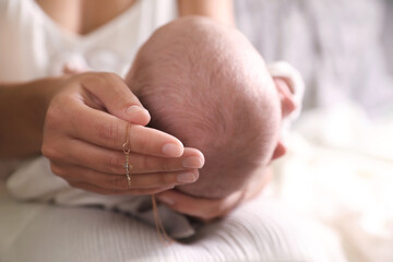 Mother holding newborn baby and Christian cross indoors, focus on hand