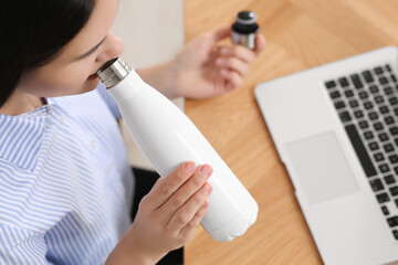Young woman drinking from thermo bottle at workplace indoors, above view - obrazy, fototapety, plakaty