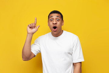 young surprised guy african american in white t-shirt shows thumb up on yellow isolated background