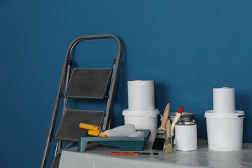 Metallic folding ladder and painting tools on table near blue wall