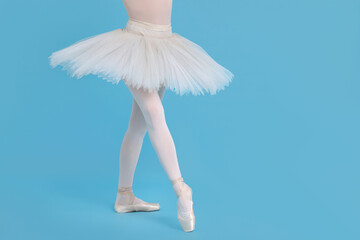 Young ballerina in pointe shoes practicing dance moves on light blue background, closeup. Space for text