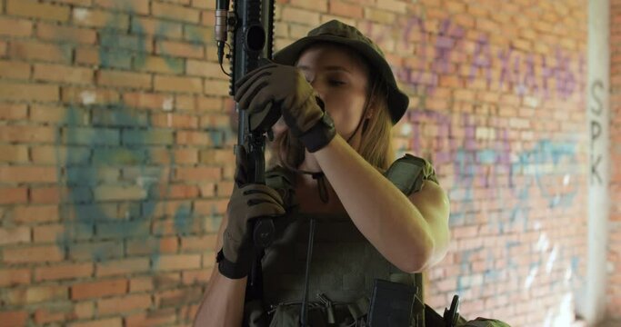 confident beautiful woman in hat loads a gun,prepares to shoot close-up slow motion. female soldier is aiming , leveling a rifle in the building slow motion camera motion