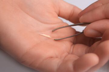 Woman pulling splinter from finger using tweezers on white background, closeup
