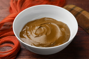 Bowl of henna cream and red strand on wooden table, closeup. Natural hair coloring
