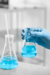 Scientist holding flask of light blue liquid in laboratory, closeup