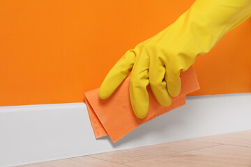 Woman in protective glove cleaning plinth with sponge cloth indoors, closeup - obrazy, fototapety, plakaty